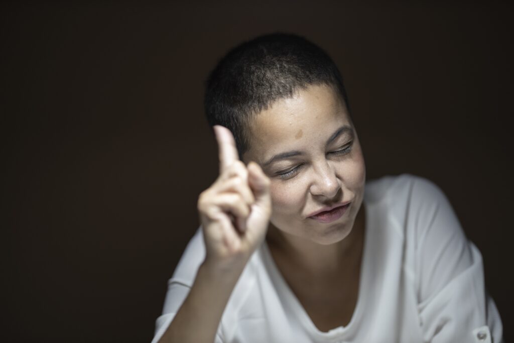 femme au cheveux courts qui baisse les yeux et fait signe avec son doigt comme pour dire qu'elle a un probleme